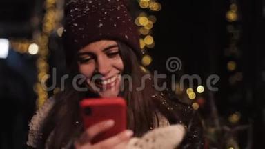 在社交网络上，戴着冬帽的微笑迷人的女孩，用智能手机，看着屏幕