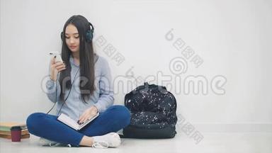 启发年轻的亚洲女孩坐在地板上，做作业，听音乐，切换歌曲，跳舞。