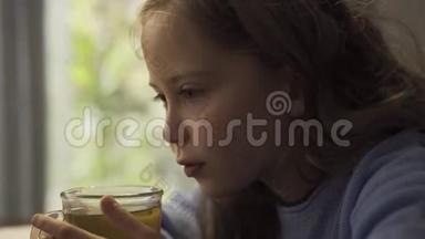 一个可爱的灰眼小女孩的特写，桌前端着一杯热茶。 白种人儿童享受热饮