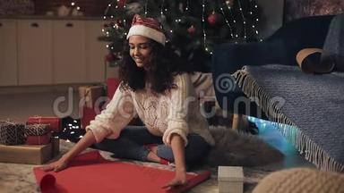 年轻漂亮的桑塔斯帽木乃托女孩<strong>坐在</strong>装饰过的圣诞<strong>树下</strong>展开纸卷，把