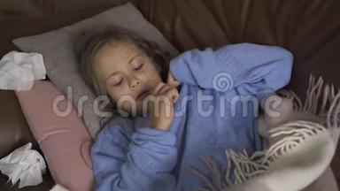 生病的年轻女孩在家里躺在毯子下面用温度计<strong>测量体温</strong>。 孩子发烧了