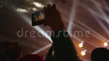 摇滚音乐音乐会上的一位女士在她的智能手机上拍摄一段视频。 会所大气，射线的五彩光芒.. 关门