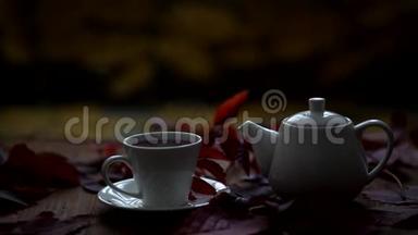 <strong>桌子</strong>上是热茶和茶壶，蒸汽来自一个杯子。 <strong>桌子</strong>上摆着一副野葡萄秋叶的装饰.. 秋天