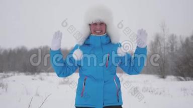 戴着温暖帽子的快乐女孩挥动双手，在白雪的背景下在冬天笑。 冬天有趣的人。 生活