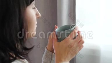 那个女孩正拿着一杯热茶或咖啡。 一个女人在看着窗外的时候喜欢喝热饮料。 穆迪