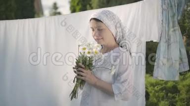 可爱的成熟女人，头上戴着白色披肩，在户外的晾衣绳上撕下雏菊花瓣。 华盛顿。 积极正面