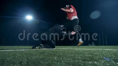 两名美式足球运动员在球场上奔跑，踢美式足球，侧视。