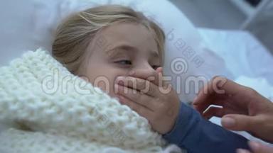 戴围巾的可爱的女孩子在床上咳嗽，慈爱的母亲<strong>抚摸</strong>着孩子的额头