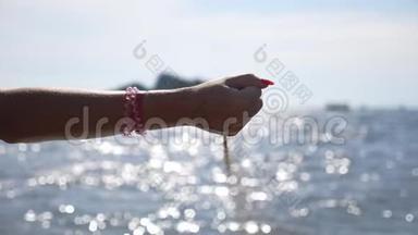 女人手里拿着一把沙子。 母臂浇黄色干沙<strong>抵御</strong>海景.. 海面上闪耀着