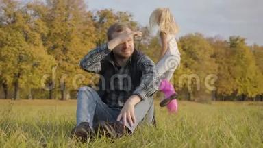 微笑的白种人女孩穿着休闲服和粉红色的橡胶靴，跑到一个男人坐在秋天的草地上。 金发美女