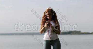 戴着白色耳机的红头发女孩正在手机上选择和听歌。