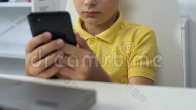 小男孩<strong>坐在</strong>笔记本<strong>电脑前</strong>，在智能手机上看视频，上瘾
