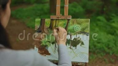 一个年轻的黑发女孩在森林里画了一幅画。 油画布上的风景。