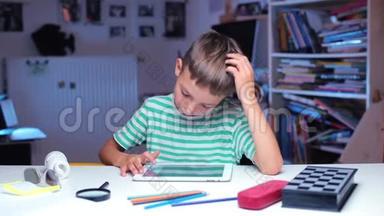 一个男孩坐在课桌旁，用手指在平板电脑屏幕上摩擦