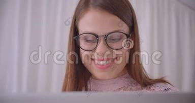 年轻漂亮的白种人女商人戴着眼镜，在<strong>笔记本</strong>电脑上打字，兴高采烈地坐在<strong>上面</strong>