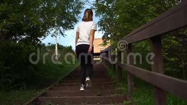 年轻漂亮的运动女孩穿着白色T恤，穿着黑色运动裤，跑上楼梯慢动作