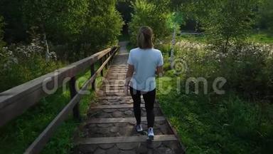 年轻漂亮的女孩或穿着白色T恤和黑色<strong>运动裤</strong>的女人在公园日落时走下楼梯。