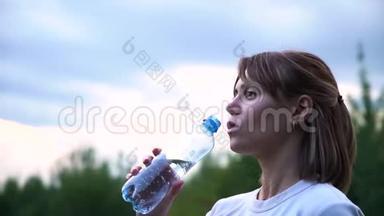 年轻漂亮的运动女孩穿着一件白色T恤，<strong>很累</strong>，喝着透明瓶子里的水，慢动作
