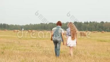 十几岁的女孩和男孩在干草堆背景下的收割场上散步。 快乐的女孩和男孩在乡下玩