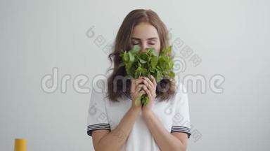 年轻漂亮的女人嗅着站在现代厨房餐桌前的新鲜绿色。 健康食品的概念.. 职业