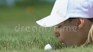 女高尔夫球初学者躺在草地上，把球吹入洞中，玩得很开心