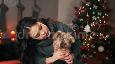 在新年圣诞节室内的亚洲年轻女子和有趣的小狗玩耍。 家庭舒适的概念，新年和