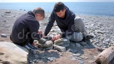 爸爸和儿子在海边的石头海滩上用木棍点燃篝火上的煤。