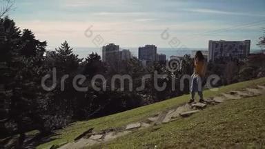女孩跑下石阶，在一座绿色的小山的背景上的高层建筑，周围是绿色植物