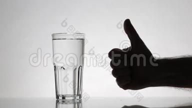 屏幕左边是一杯水。 一个男人`他的手从<strong>镜框</strong>后面伸出来，竖起大拇指
