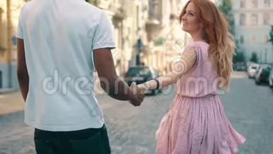年轻快乐的女人牵着男友`手沿着城市街道，后视