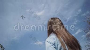 金色长发的女孩抬头望着那架载着云彩在蓝天上飞行的飞机