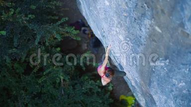俯视女子攀岩者在艰难的运动路线上攀爬，攀岩者休息，粉笔手挂在悬崖上。