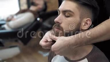 理发师的特写与一个长胡子的英<strong>俊男</strong>子做造型。 理发师在工作过程中`手。 Barbe