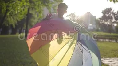 五颜六色的伞躺在公园的草地上。 一个无忧无虑的小男孩从伞后面<strong>跳出</strong>来