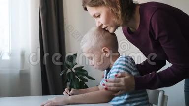 小男孩，孩子，坐在家里的桌子旁画画，妈妈亲吻拥抱他
