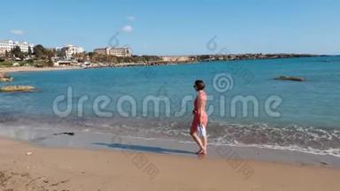 年轻迷人的孤独女孩走在海边的沙滩上。 漂亮的白种人女人穿着红色的衣服在海边散步。 裸舞