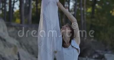 微笑的白种人女人站在森林里，戴着被风吹过的浅白色围巾，抬头看着。 漂亮姑娘