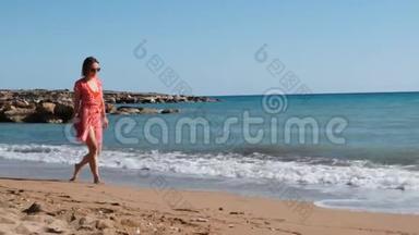 年轻迷人的女孩穿着红色<strong>短裙</strong>沿着大海散步。 白人黑发女人走在沙滩上。 穿红色衣服的年轻女孩
