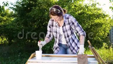 成人手工艺妇女在夏季果园里用白色油漆画木木板