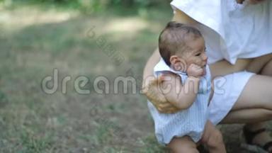 年轻漂亮的母亲穿着一件白色的衣服，教她刚出生的女儿在公园里的一片新鲜的绿草上行走。 母亲和