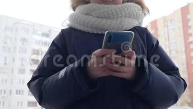 青少年女孩在冬天散步时使用<strong>手机</strong>。 将手持智能<strong>手机</strong>的少年女孩举在住宅的冬<strong>季</strong>街道上