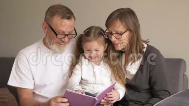 可爱的祖父母和他们的孙子坐在书上一起读有趣的故事的画像