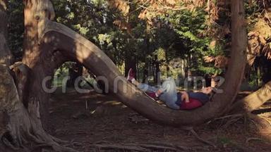 一个可爱的女孩躺在公园的一棵大树的半圆形树干上半圆形树干上休息