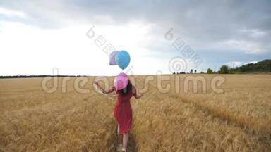 快乐的女孩穿着红色的的快乐女孩手里拿着气球穿过金色的麦田。 年轻女子棕色