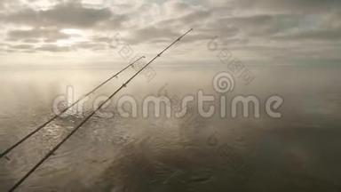三根鱼竿在水面上的景色，钓船上挂着尖嘴。 多云的天空在背景上。