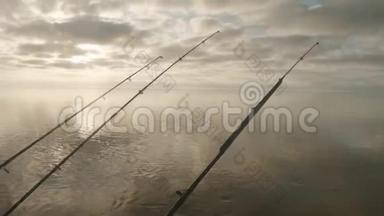 <strong>三根</strong>鱼竿在水面上的景色，钓船上挂着尖嘴。 多云的天空在背景上。