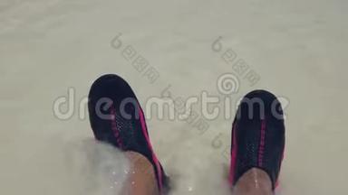 穿着泳鞋站在白色沙滩上的男子脚上翻滚波浪的特写镜头