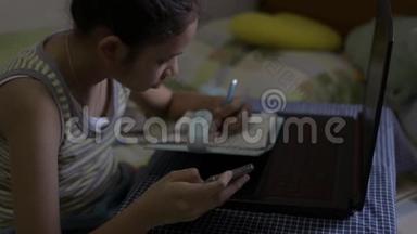 亚洲可爱的女孩穿着单身衬衫在<strong>网上</strong>看课，在床上做作业。 女青少年在家<strong>学习</strong>。