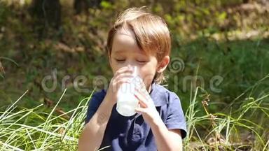 快乐的笑男孩在大自然的背景下喝牛奶或酸奶。 儿童天然健康食品..