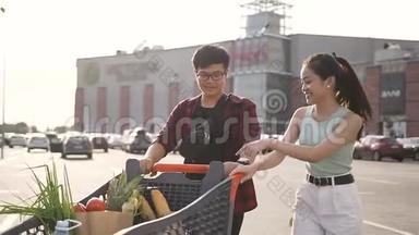 快乐迷人的亚洲夫妇被推到他们面前一辆装满各种产品的手推车